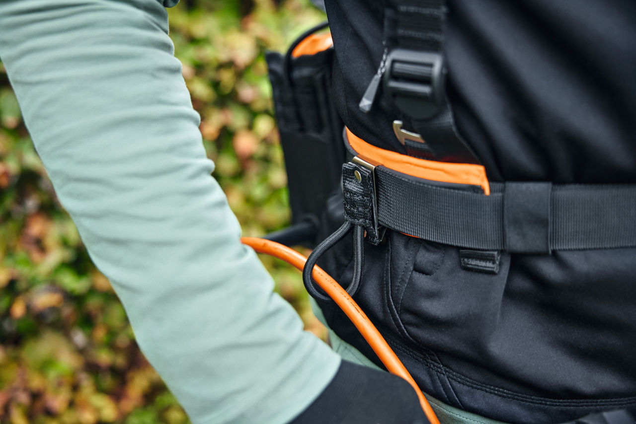 Човек носи модулната система колани STIHL ADVANCE X-Flex с чанта за акумулаторна батерия със захранващ кабел и водач за кабел