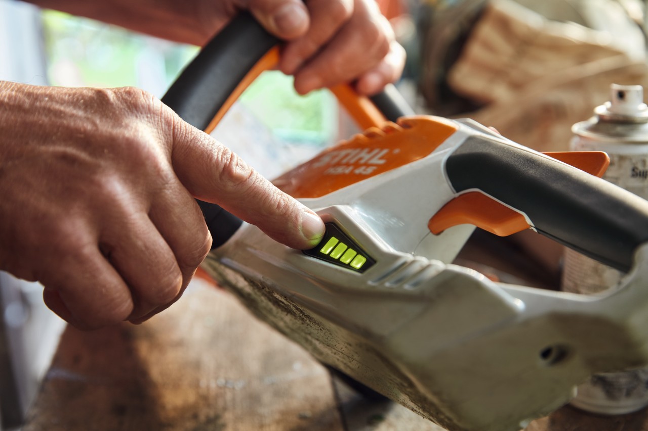 Човек проверява нивото на зареждане на акумулаторната тример за жив плет STIHL HSA 45.