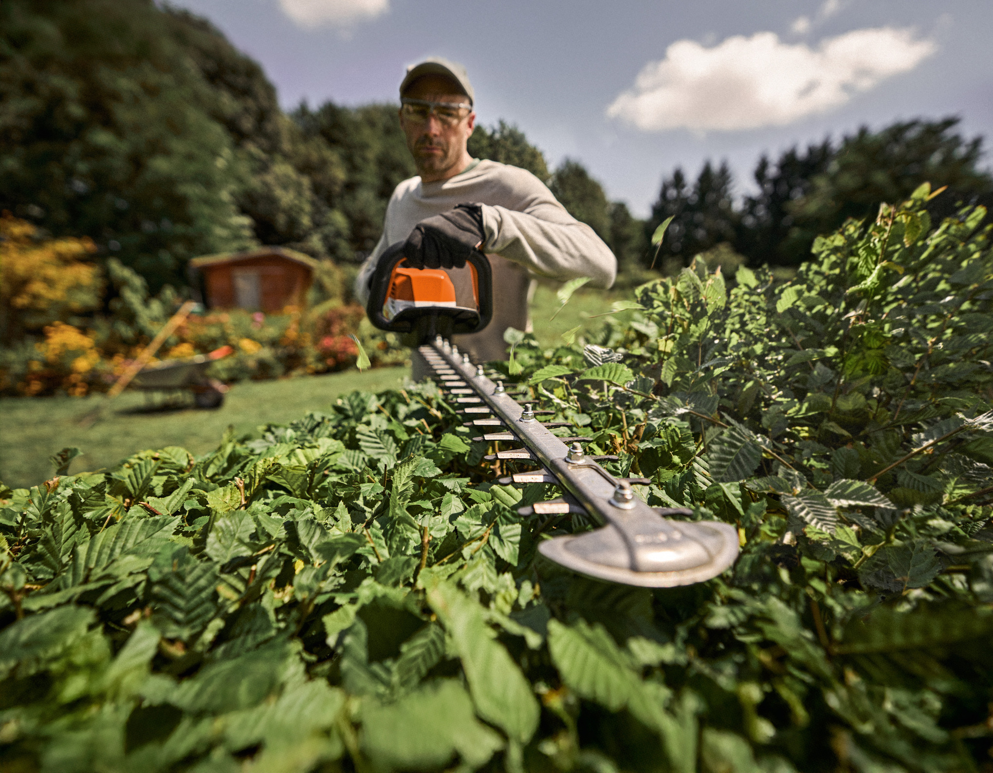 Мъж с ножица за жив плет в ръка се разхожда в градина