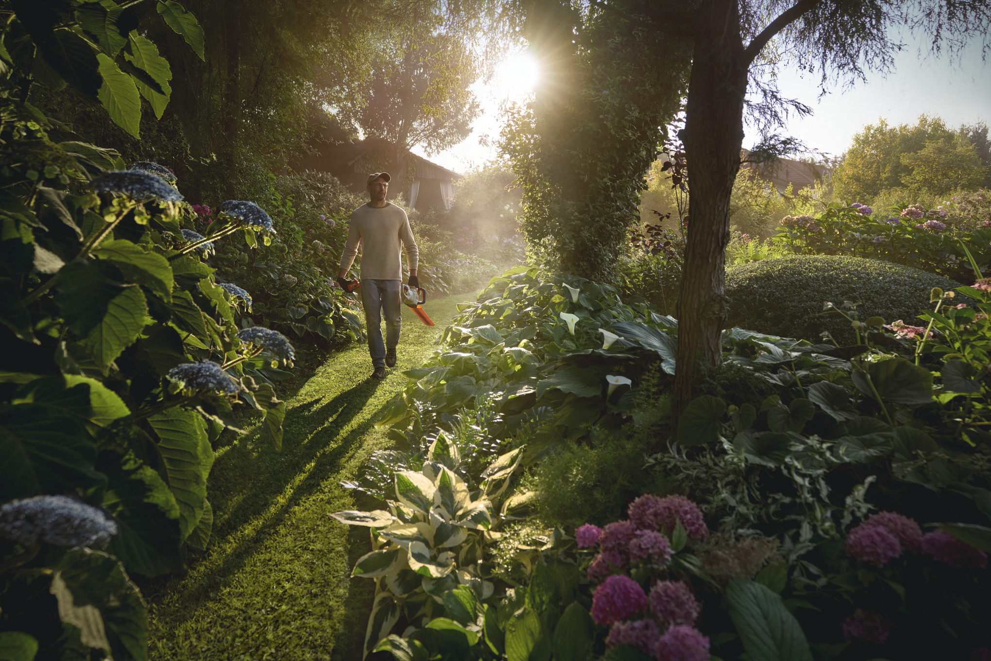 Мъж с ножица за жив плет в ръка се разхожда в градина