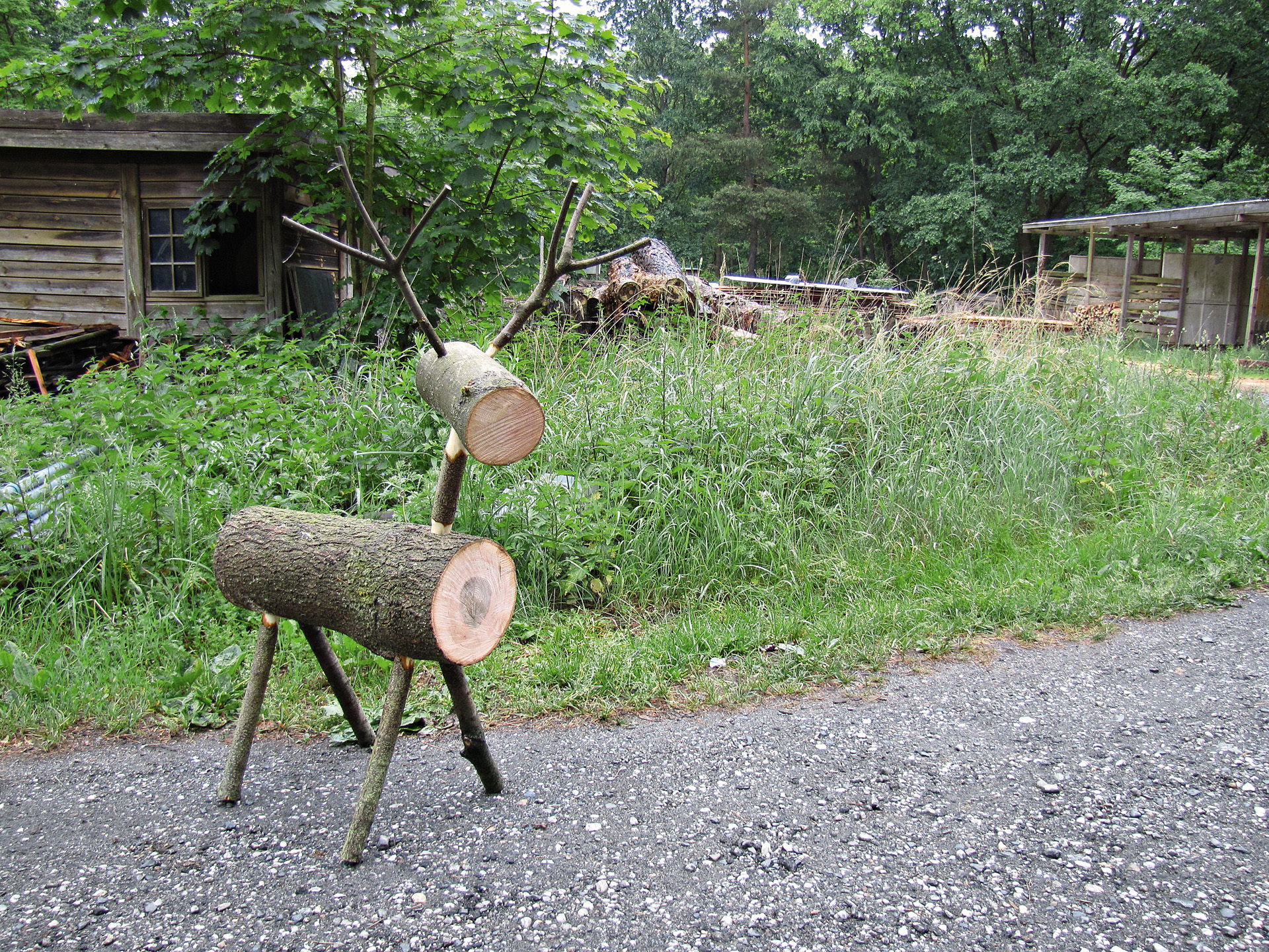Дървен северен елен пред зелена морава и дървена хижа