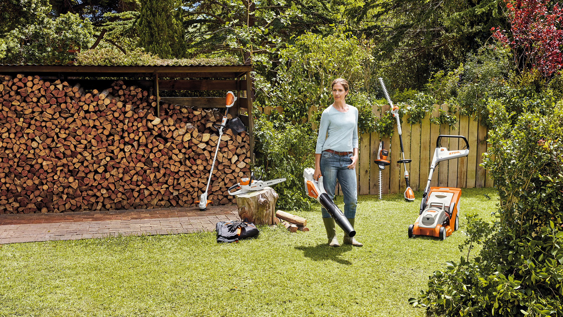 Жена стои в градината пред купчина дърва с уреди от системата AK 