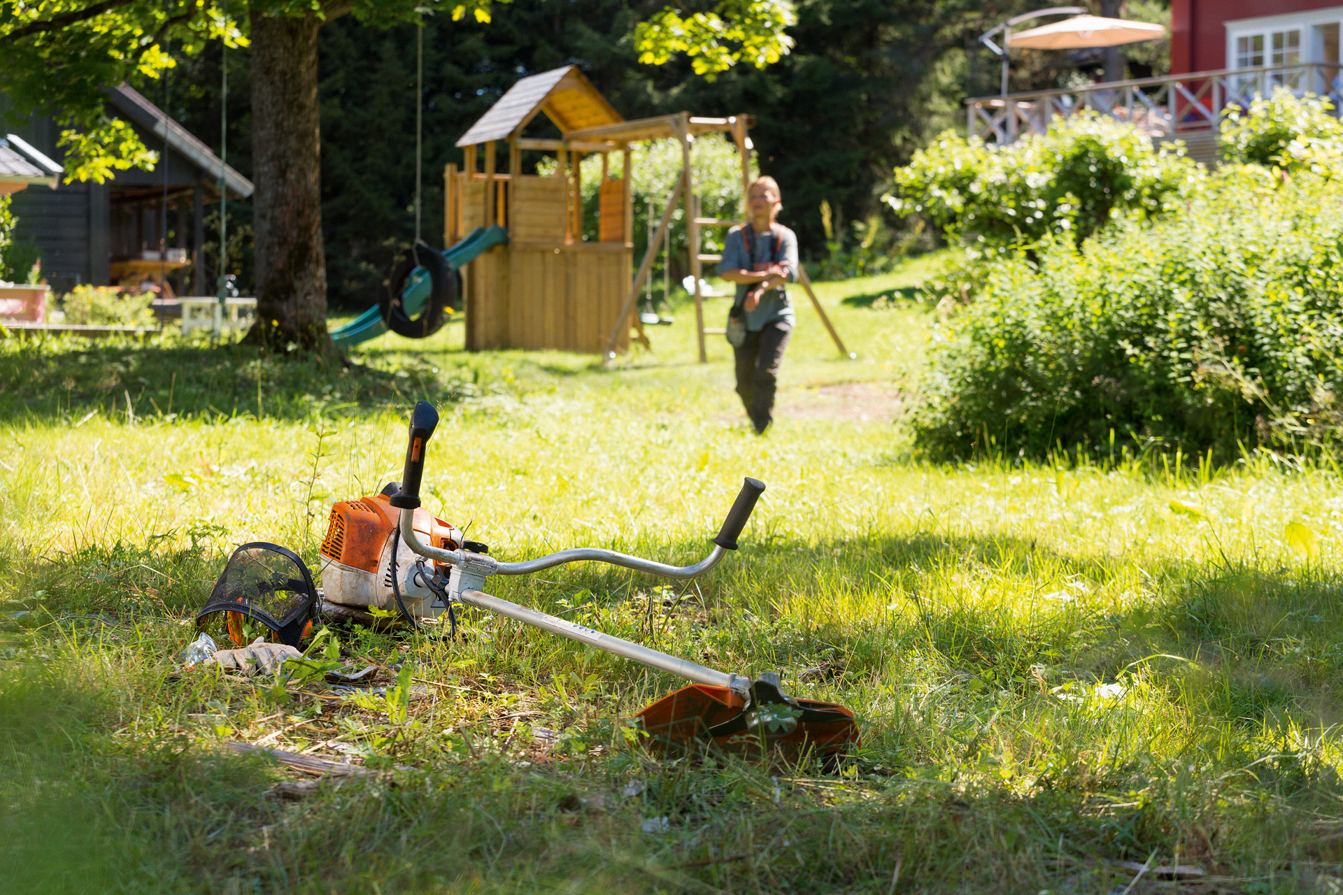 Моторна коса STIHL FS 240 е положена на тревата, на заден план жена се приближава за извършване на техническо обслужване 