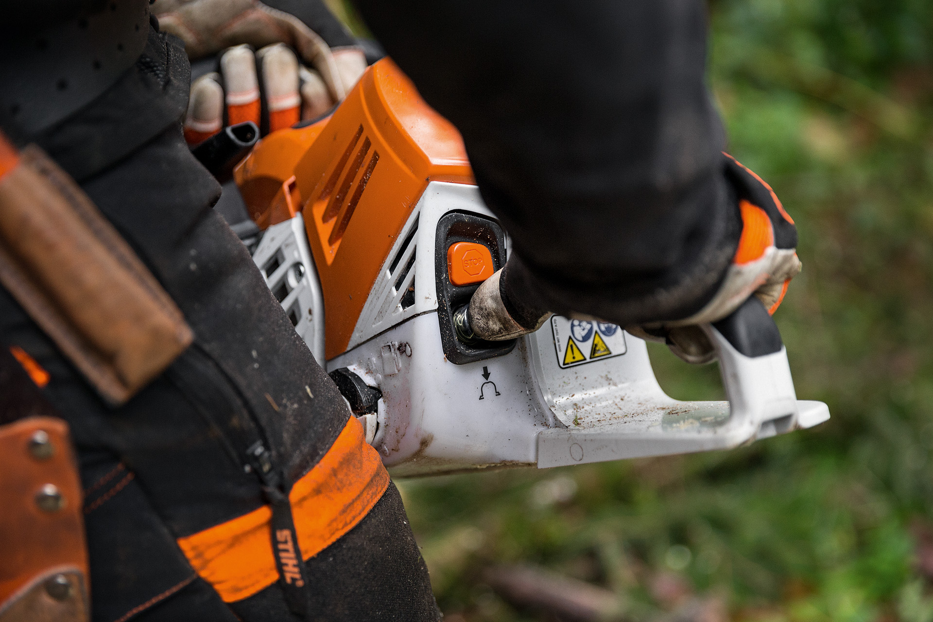 Човек в предпазно облекло стартира бензинов верижен трион STIHL MS 500i в разлистена гора на земята